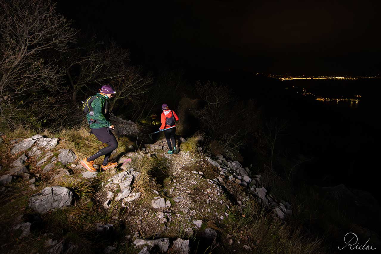 Runner con lampada frontale su un tratto roccioso ed esposto durante una partenza notturna della Corsa della Bora