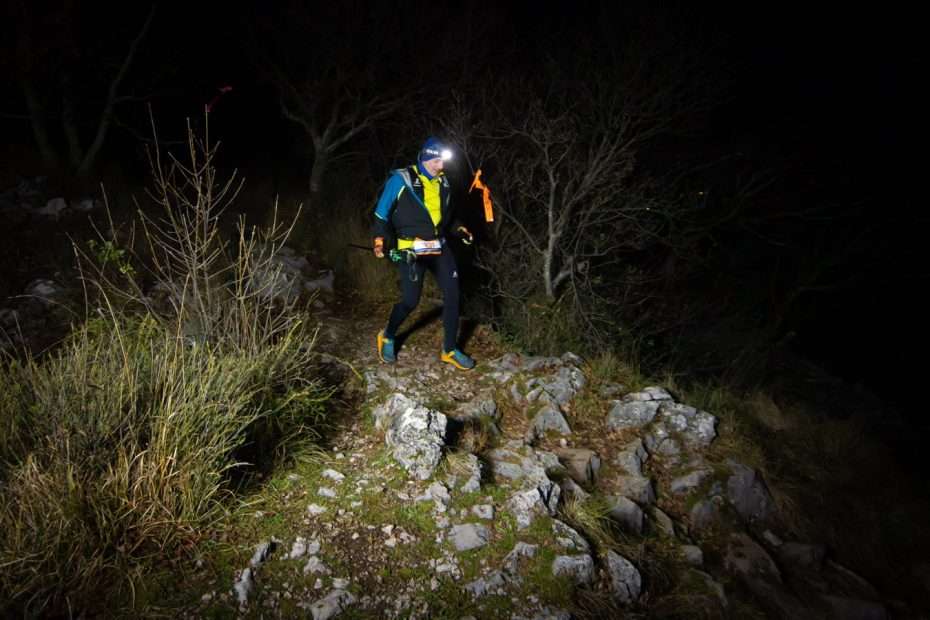 A runner with a head torch on the rocky trail at night, during the Corsa della Bora