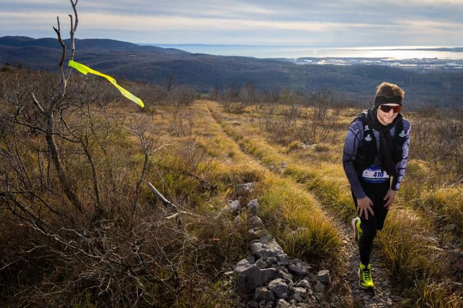 A runner climbing the border path, with the plain and the sea at Monfalcone behind